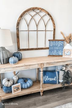 a wooden table topped with blue and white pumpkins next to a large arched window