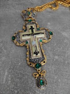 an ornate cross with green stones and gold chains on a gray surface, next to a golden chain