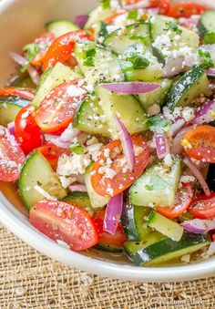 a white bowl filled with cucumber, tomatoes and onions on top of a table