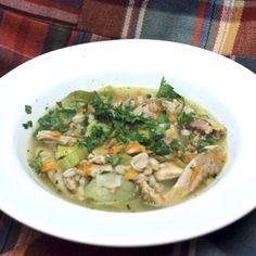 a white bowl filled with soup sitting on top of a plaid tablecloth covered table