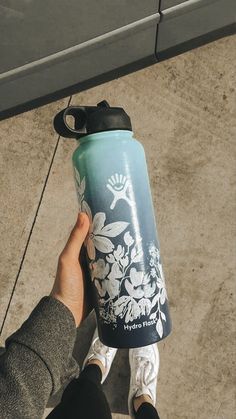 a person holding a blue and white water bottle with flowers painted on the side, while standing in front of a building