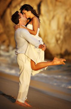 a man and woman are dancing on the beach at sunset with their arms around each other