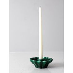 a white candle sitting in a green bowl with a long pillar sticking out of it