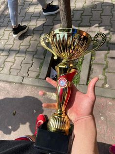 a person holding up a gold trophy in their hand on the sidewalk next to a tree