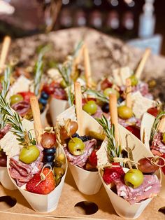 an assortment of appetizers are arranged in small cups with olives, strawberries, and meat