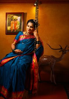 a woman in a blue sari sitting on a swing next to a deer statue