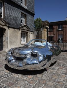 a silver car parked on top of a cobblestone road next to a building