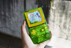 a person holding up a green and yellow gameboy with an ad on the screen