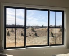 an empty room with three large windows overlooking a field and trees in the foreground