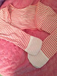 a pink and white striped shirt laying on top of a bed next to a pillow