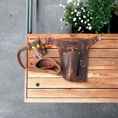 a wooden bench with two brown leather bags on it's back and flowers in the background