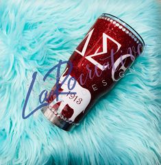 a red glitter tumbler sitting on top of a blue fuzzy blanket