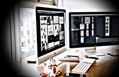 two computer monitors sitting on top of a wooden desk next to each other in front of a window