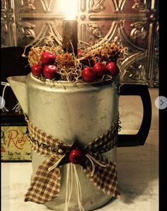 a candle is lit in an old tin can with cherries and pine cones on it