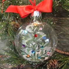 a glass ornament with a red bow on it's neck and tree branches in the background