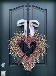 a heart - shaped wreath with an arrow and bow hangs on the front door's black door