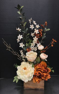 an arrangement of white and orange flowers in a wooden vase on a black table top