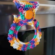 a multicolored knitted wreath hanging on a stove door handle with an orange button