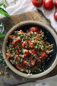 a bowl filled with tomatoes and other vegetables on top of a wooden cutting board next to green leaves