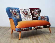 an orange and blue couch sitting on top of a hard wood floor next to a white wall