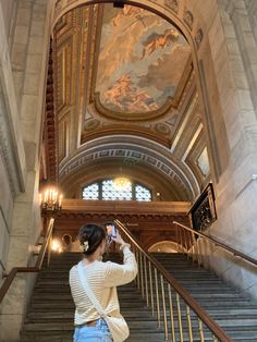 a woman taking a photo on her cell phone while standing at the top of some stairs