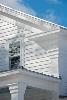 the corner of a white house with a clock on it's side and a blue sky in the background