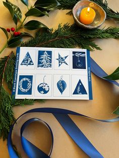 a christmas card with blue ribbon and decorations on it, next to a lit candle