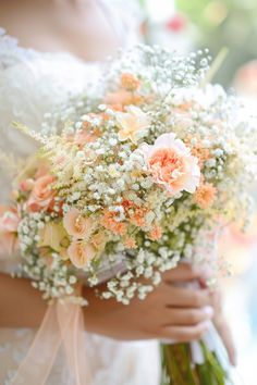 a bride holding a bouquet of white and peach flowers on her wedding day in front of a window