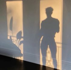 the shadow of a man standing in front of a window next to a chair and desk