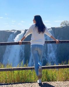 a woman standing at the edge of a cliff looking out over a waterfall with her arms outstretched