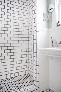 a bathroom with black and white tiles on the shower wall, sink, and mirror