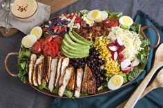 a large salad with chicken, avocado, tomatoes, black beans and eggs