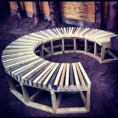 a circular bench made out of wooden planks in the middle of some dirt and trees