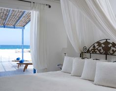 a bed with white sheets and pillows in front of an open door to the beach