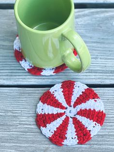 a cup and coaster sitting on top of a wooden table next to a green mug