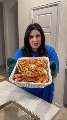 a woman holding a tray of cooked crabs in her hands and looking at the camera