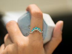 a woman's hand holding an open ring with turquoise stones on the inside of it