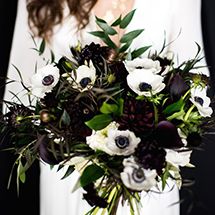 a woman holding a bouquet of white and black flowers with greenery in her hands