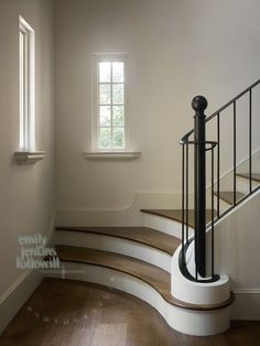 a white staircase with wooden handrails next to a window in an empty room