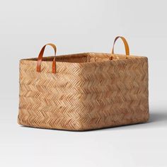 a large woven basket with leather handles on the bottom and sides, sitting on a white surface