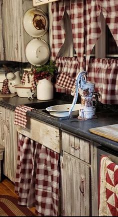 an old fashioned kitchen with red and white checkered curtains hanging from the window over the sink