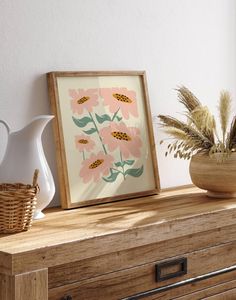 a wooden dresser topped with a vase filled with flowers next to a framed art print