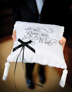 a person in a suit holding a white pillow with black ribbon and writing on it