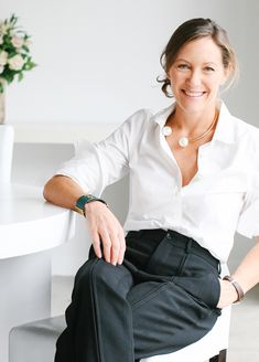 a woman is sitting on a chair smiling for the camera while wearing black slacks and a white shirt