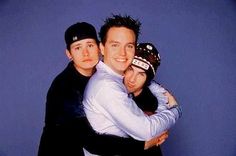 two men hugging each other in front of a blue background with one man wearing a hat