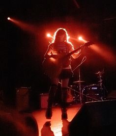 a woman on stage with a guitar in front of her and some lights behind her