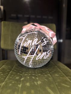 a shiny disco ball sitting on top of a green chair with a pink ribbon around it