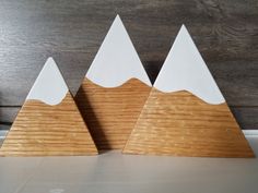 three wooden mountain sculptures sitting on top of a white counter next to a wood wall