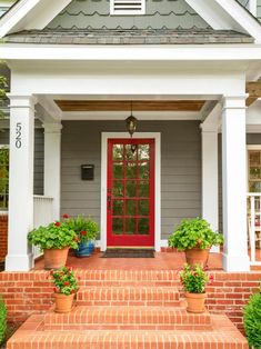 a red front door on a house with potted plants in the foreground and brick steps leading up to it