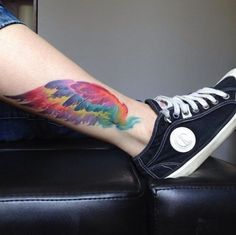 a person with a colorful tattoo on their leg sitting on a black leather couch next to a wall